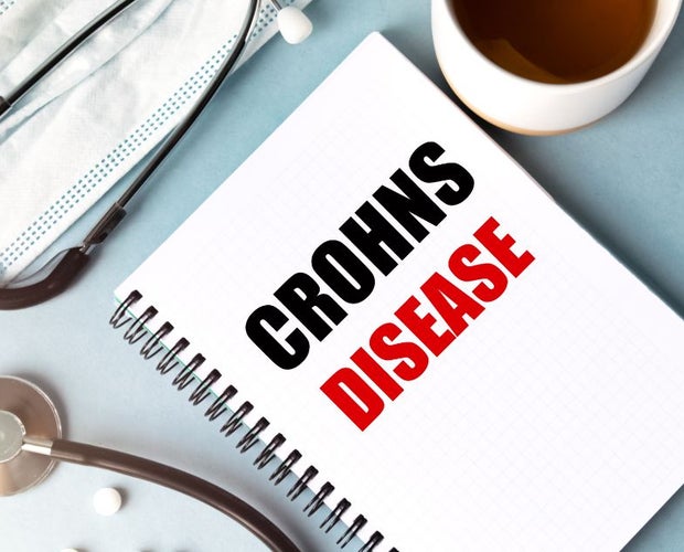 Featured image for an article on cannabis for Crohn's disease. A textbook with the text Crohn's disease sits on a desk next to medical equipment.